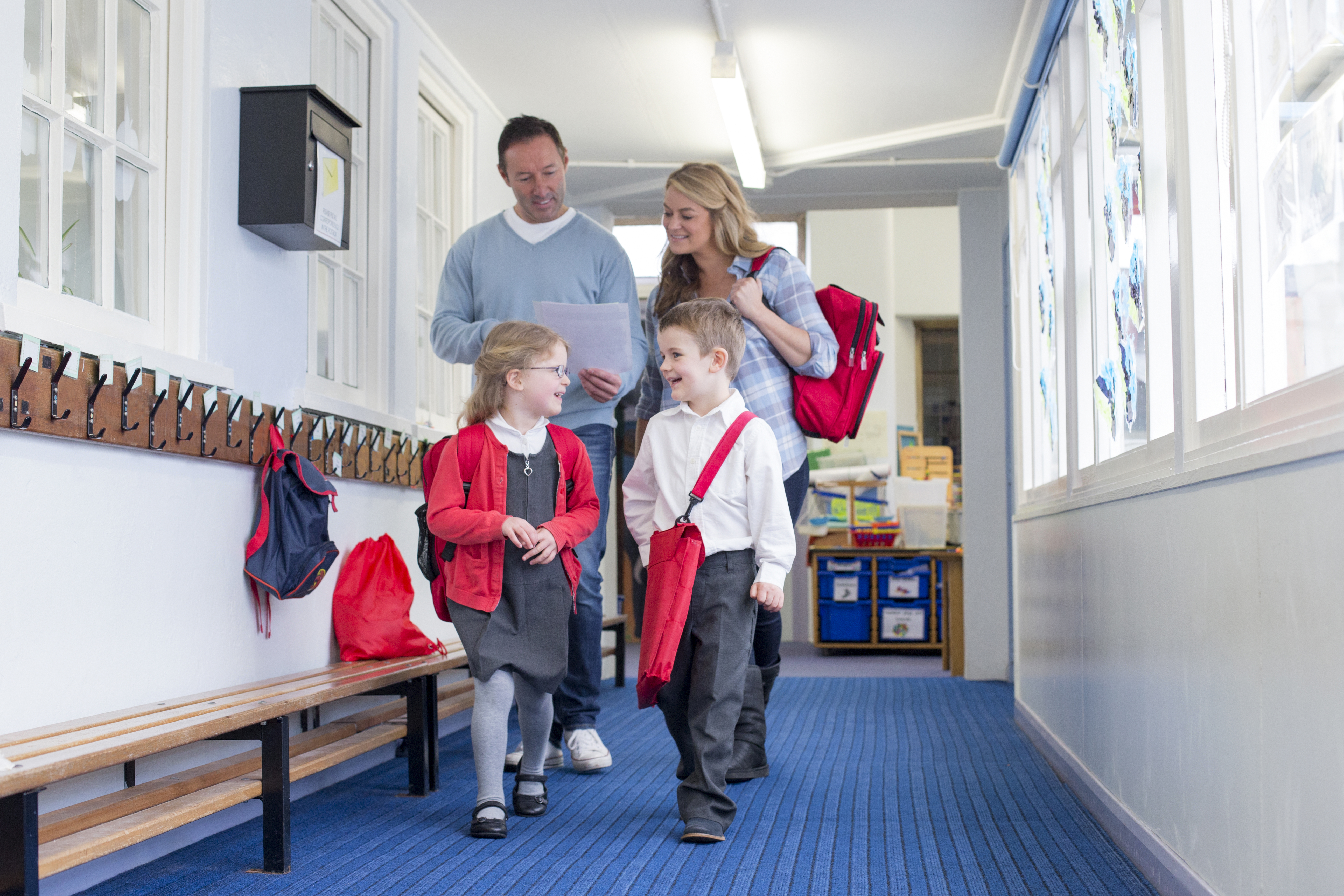 Parents and students walking down a primary school corridor. the parents are looking at some paperwork and the children are talking.