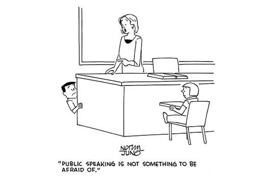 A boy is crouching behind his teacher's desk. The teacher says to him, "Public speaking is not something to be afraid of."
